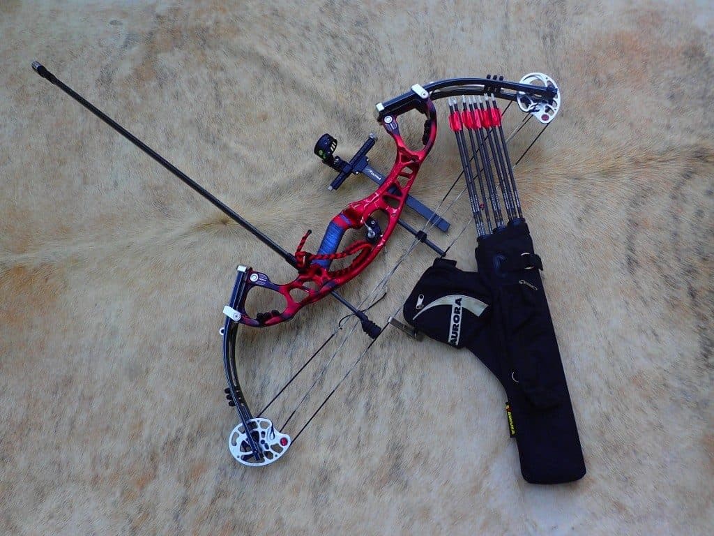 A compound bow with sight and stabiliser laid out beside a quiver of arrows