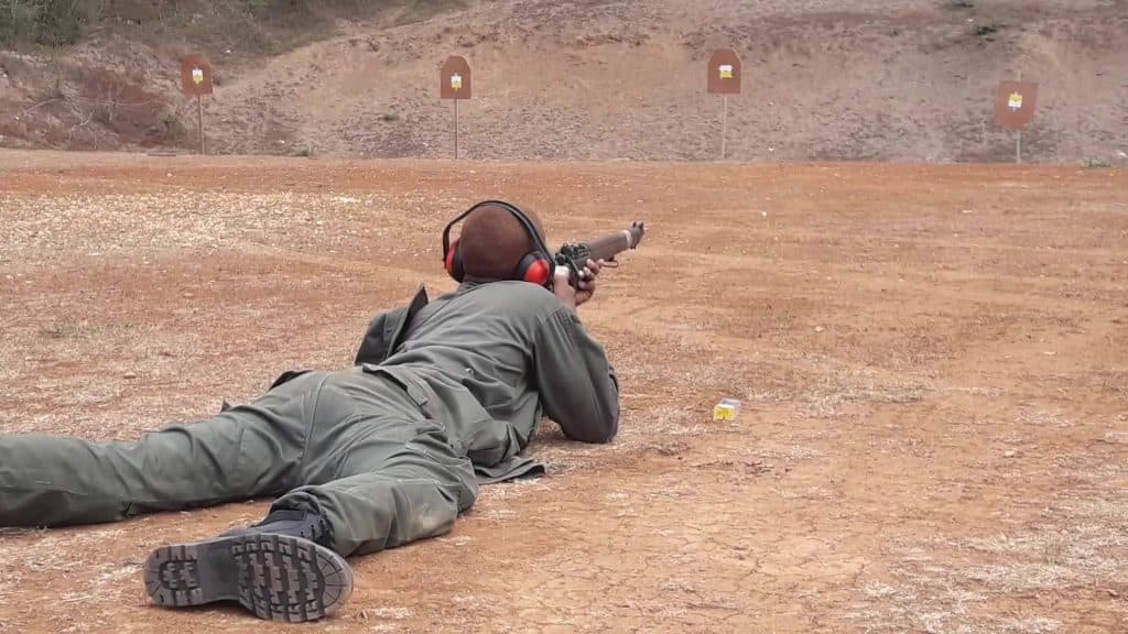 A cadet in fatigues and ear defenders shooting prone at a row of cardboard targets set against an earth bank