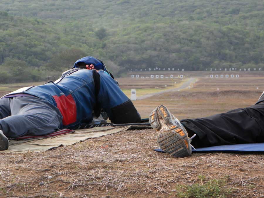Two shooters lying prone on the mound, looking down a wide range at a distant line of numbered targets