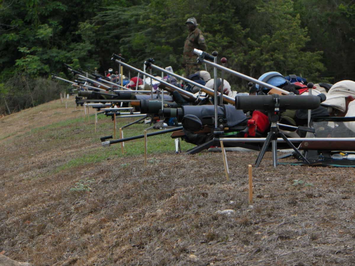 A line of full bore rifles and spotting scopes set up along the firing mound, a range officer walking behind the point