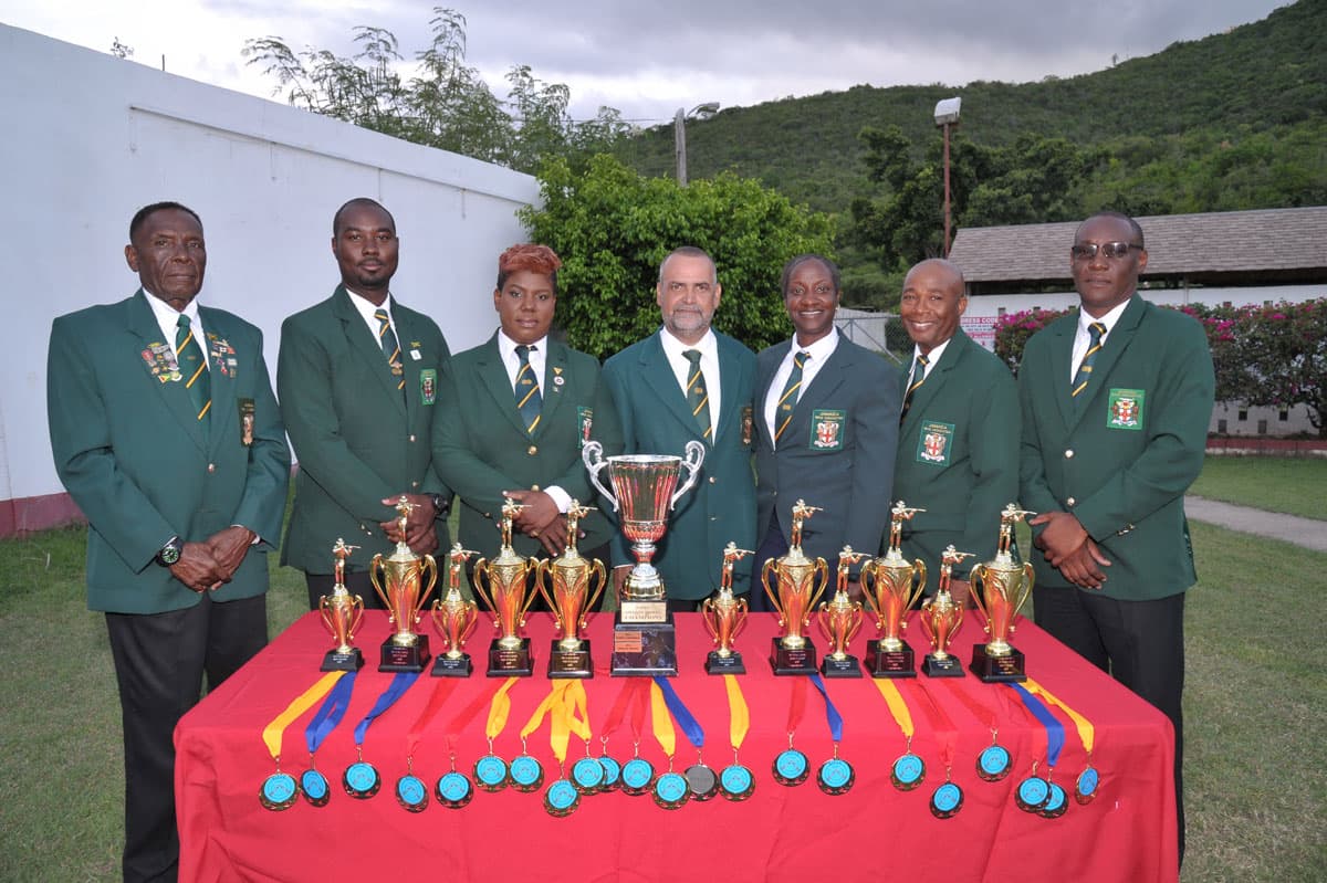 Seven shooters in the association’s green blazers standing behind a table of trophies and medals