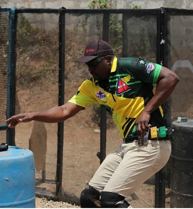 A competitor reaching out to pull a stage activator, pistol holstered, mid-stage between two barrels