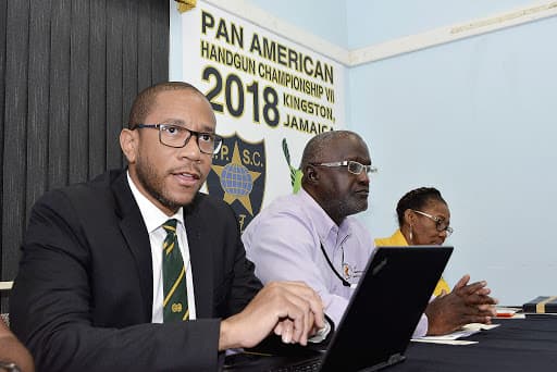 Three association officials at a table at the launch of the Pan American Handgun Championship VII, under a backdrop reading Kingston, Jamaica 2018